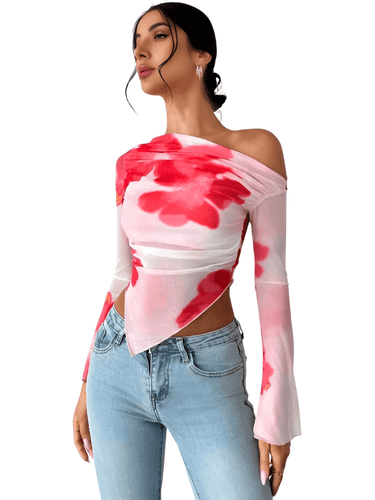A woman wearing an asymmetrical off-the-shoulder top with long sleeves and a floral pattern in pink and brown colors, paired with blue denim jeans.